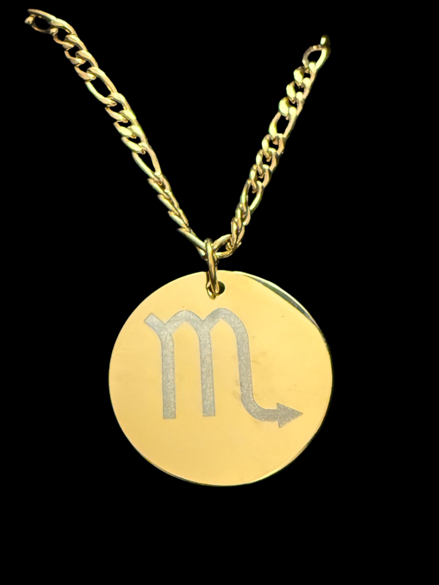 Gold necklace with a pendant featuring a astrological symbol on a black background.