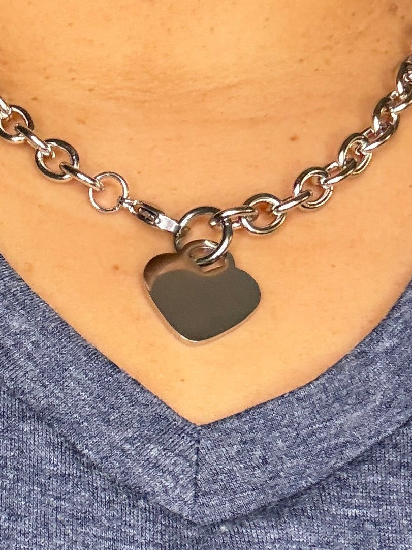 Close-up of a person wearing a silver chain bracelet with a heart-shaped pendant.