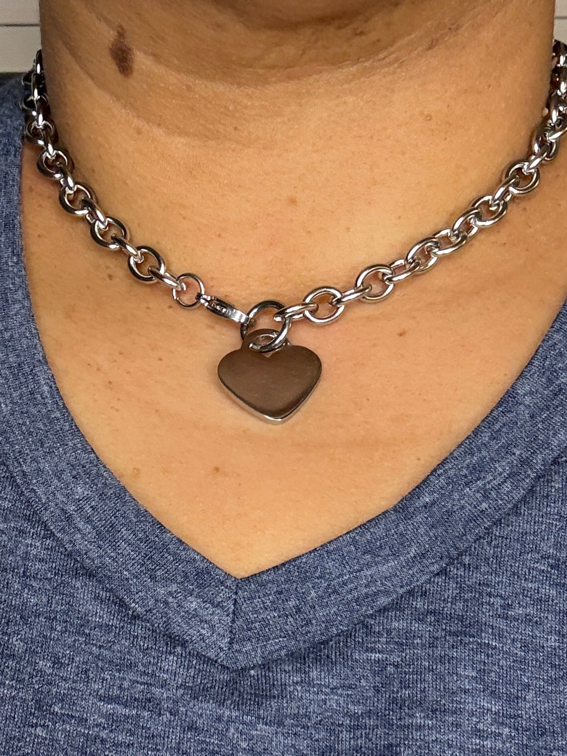 Person wearing a blue shirt with a heart-shaped pendant on a chain.
