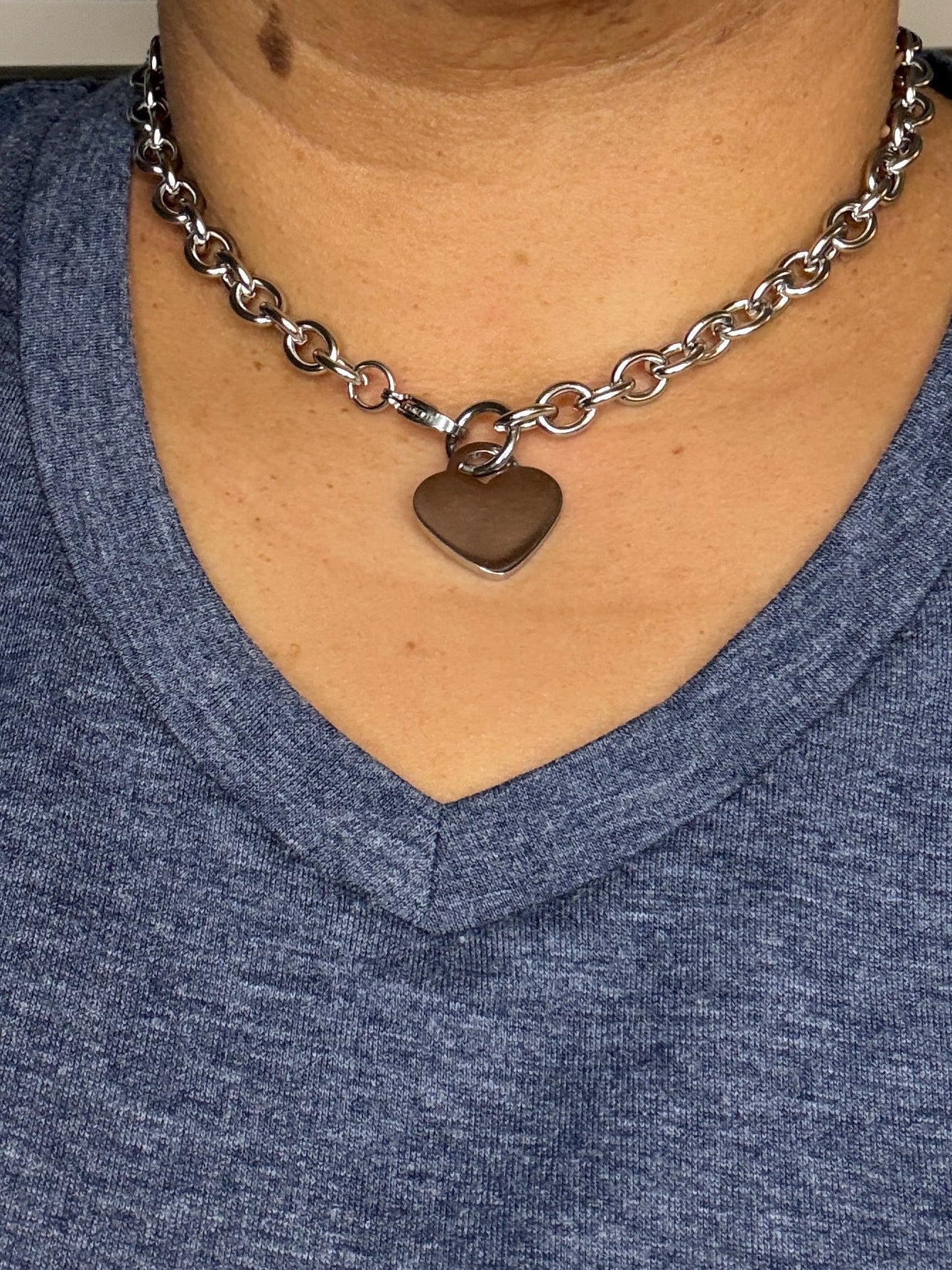 Person wearing a blue shirt with a heart-shaped pendant on a chain around their neck.